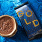 Ceramic mug with hot cacao and a package of Amazonian Gold Legacy Cacao on a blue textured background